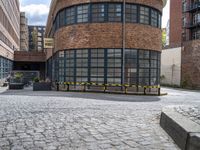 a brick and iron building sitting on the side of a road next to a black and yellow bench