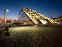 a very modern building next to a river with some lights on it at nighttime