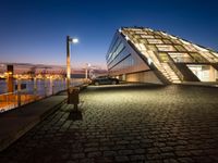 a very modern building next to a river with some lights on it at nighttime