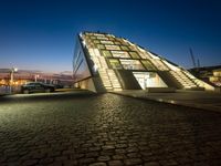 a very modern building next to a river with some lights on it at nighttime