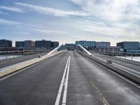 a very long bridge over water with buildings in the background at day time with clouds and sunbeams