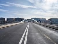 a very long bridge over water with buildings in the background at day time with clouds and sunbeams