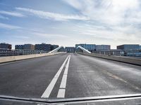 a very long bridge over water with buildings in the background at day time with clouds and sunbeams