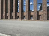 a large brick building near a parking lot on the side of the road with a blue sky and clouds reflected in the windows