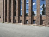 a large brick building near a parking lot on the side of the road with a blue sky and clouds reflected in the windows