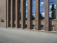 a large brick building near a parking lot on the side of the road with a blue sky and clouds reflected in the windows