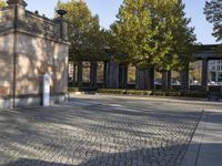 a concrete pillar on a stone floor with a green fence around it and buildings in the background