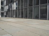 a sidewalk with two white fire hydrants outside of a building with windows in it