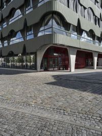 a large curved office building with several windows and doors in front of it and cobbles on either side