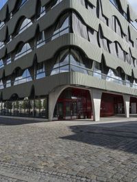 a large curved office building with several windows and doors in front of it and cobbles on either side