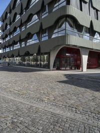 a large curved office building with several windows and doors in front of it and cobbles on either side