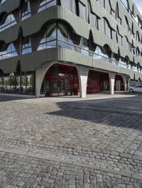 a large curved office building with several windows and doors in front of it and cobbles on either side