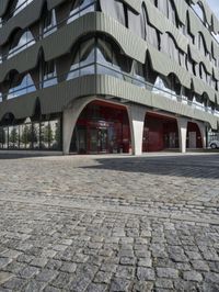 a large curved office building with several windows and doors in front of it and cobbles on either side