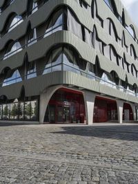 a large curved office building with several windows and doors in front of it and cobbles on either side