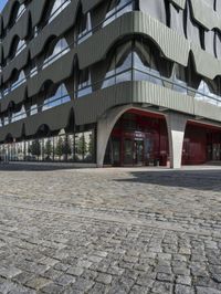 a large curved office building with several windows and doors in front of it and cobbles on either side