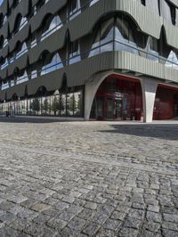 a large curved office building with several windows and doors in front of it and cobbles on either side