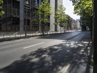 a road lined with trees in front of a tall building and another on the street with a few people riding bicycles behind it