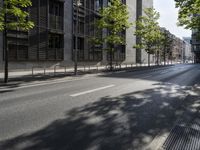 a road lined with trees in front of a tall building and another on the street with a few people riding bicycles behind it