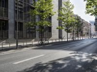 a road lined with trees in front of a tall building and another on the street with a few people riding bicycles behind it