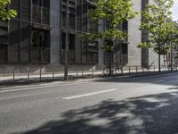 a road lined with trees in front of a tall building and another on the street with a few people riding bicycles behind it