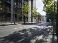 a road lined with trees in front of a tall building and another on the street with a few people riding bicycles behind it