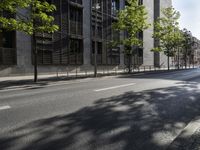 a road lined with trees in front of a tall building and another on the street with a few people riding bicycles behind it