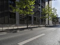 a road lined with trees in front of a tall building and another on the street with a few people riding bicycles behind it