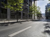 a road lined with trees in front of a tall building and another on the street with a few people riding bicycles behind it