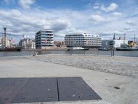 an empty cement sidewalk with some buildings in the background on a sunny day by the water