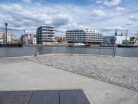 an empty cement sidewalk with some buildings in the background on a sunny day by the water