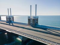 a bridge over the ocean with construction equipment in the background and two people walking on it