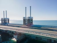 a bridge over the ocean with construction equipment in the background and two people walking on it