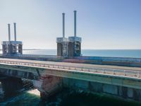 a bridge over the ocean with construction equipment in the background and two people walking on it