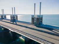 a bridge over the ocean with construction equipment in the background and two people walking on it