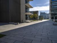 an empty stone walkway with large buildings on the sides in the background and sun beaming through the window