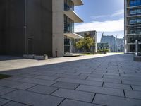 an empty stone walkway with large buildings on the sides in the background and sun beaming through the window