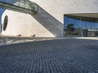 a circular stone structure with a glass facade and two benches under it on a brick walkway near a modern glass building