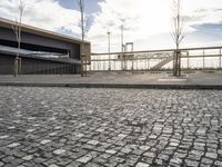 a black paved sidewalk, with an area for walking or sitting next to it and a bridge in the background