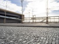 a black paved sidewalk, with an area for walking or sitting next to it and a bridge in the background