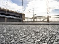 a black paved sidewalk, with an area for walking or sitting next to it and a bridge in the background