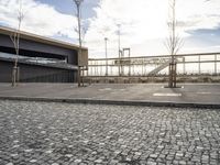 a black paved sidewalk, with an area for walking or sitting next to it and a bridge in the background