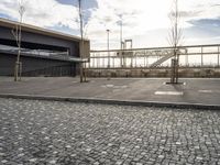 a black paved sidewalk, with an area for walking or sitting next to it and a bridge in the background