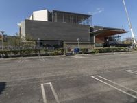 a parking lot with an empty building in the background and bushes to the side of the building