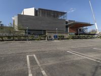 a parking lot with an empty building in the background and bushes to the side of the building