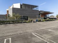 a parking lot with an empty building in the background and bushes to the side of the building