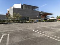 a parking lot with an empty building in the background and bushes to the side of the building