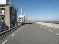 a bridge over the ocean with construction equipment in the background and two people walking on it