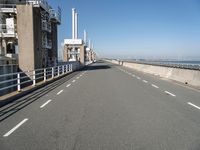 a bridge over the ocean with construction equipment in the background and two people walking on it