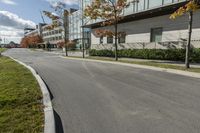 a paved road next to some buildings on a sunny day with trees in the foreground