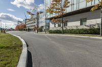 a paved road next to some buildings on a sunny day with trees in the foreground